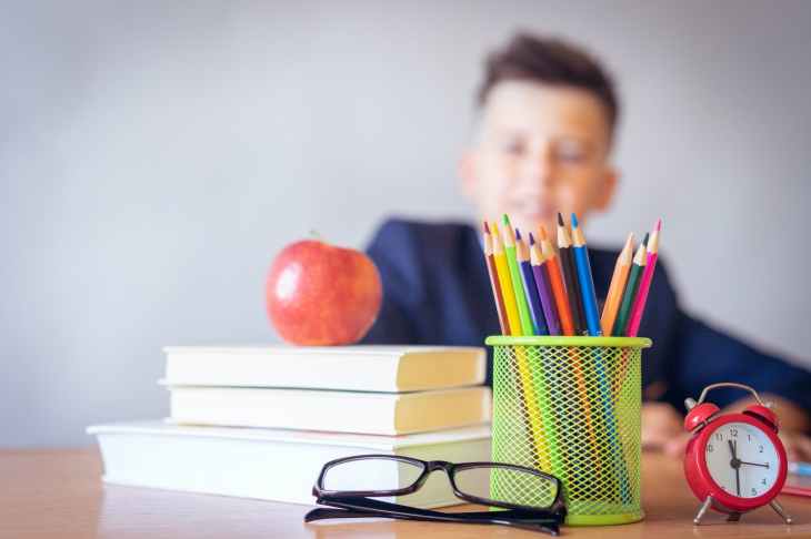 Niño detrás de un escritorio con libros, lápices y una manzana